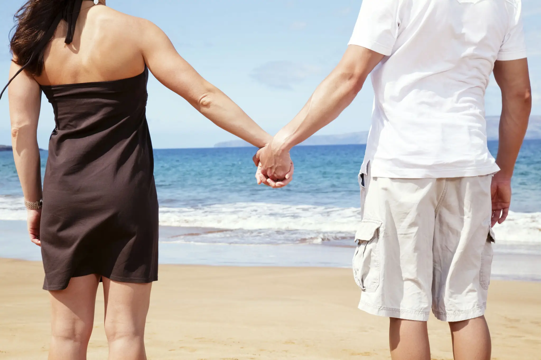 A couple holding hands on a beach with the ocean in the background.